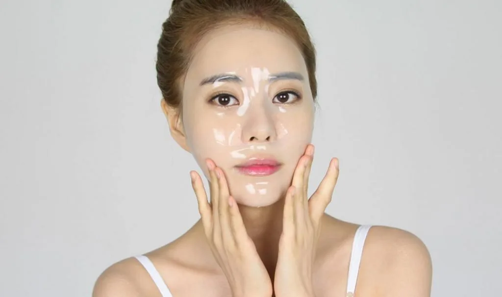 Woman smoothing a clear hydrating gel over her face as a hydration step in a Korean skincare routine
