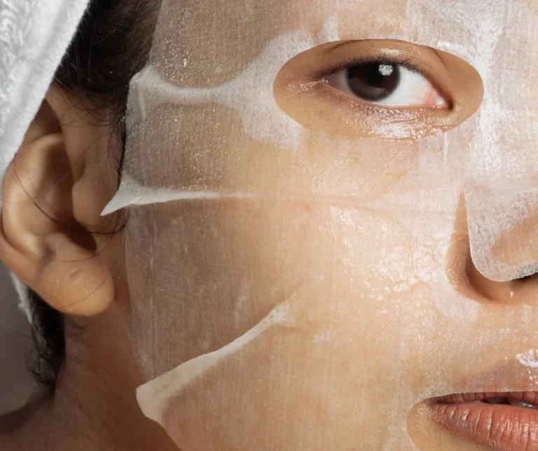 Close-up of a hydrating anti-aging sheet mask on the face, showing the serum-soaked fabric