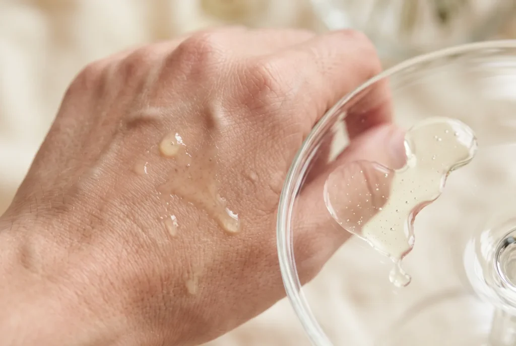 Thin, watery pale-yellow vitamin C serum drops on the back of a hand and on glass